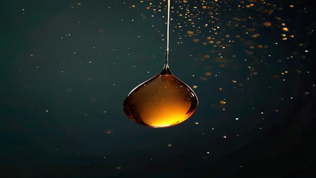 A single droplet of viscous resin suspended mid-fall against a dark background under strong directional light